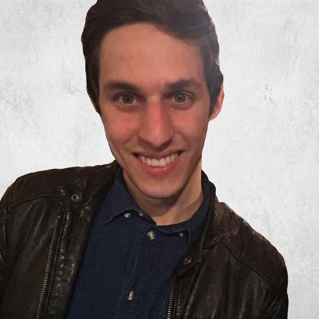 Professional portrait of young male game designer with dark hair and beard wearing black turtleneck against dark background with dramatic lighting